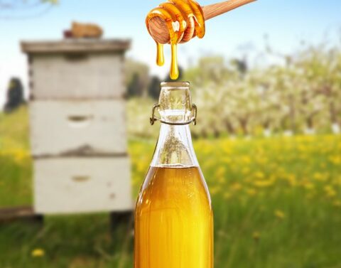 Honey dripping from a dipper into a bottle beside a hive.