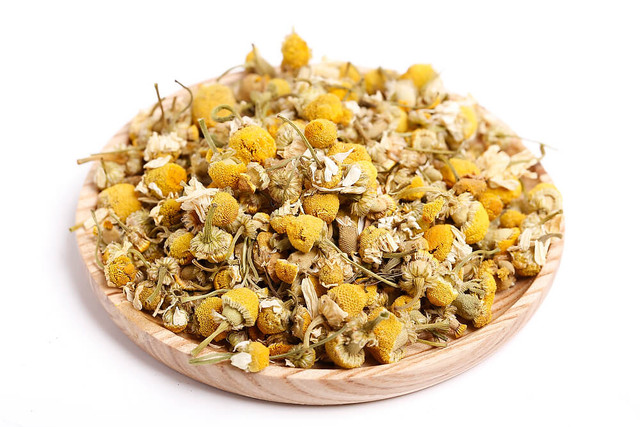 Dried chamomile flowers in a wooden dish.